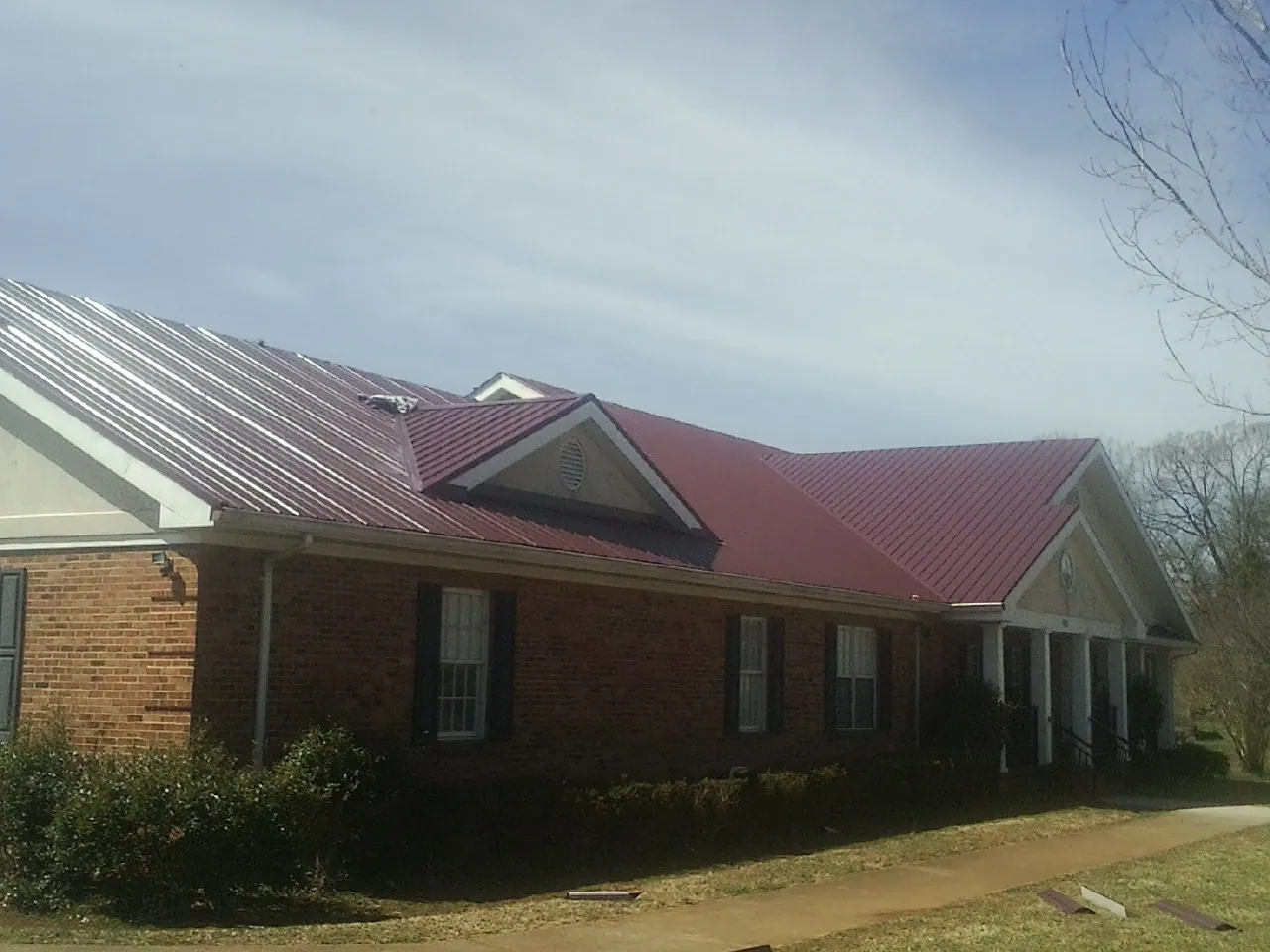 Red metal roof with gabled entries on a long brick building, from a Hail Damage Roof Repair job in Cranbury