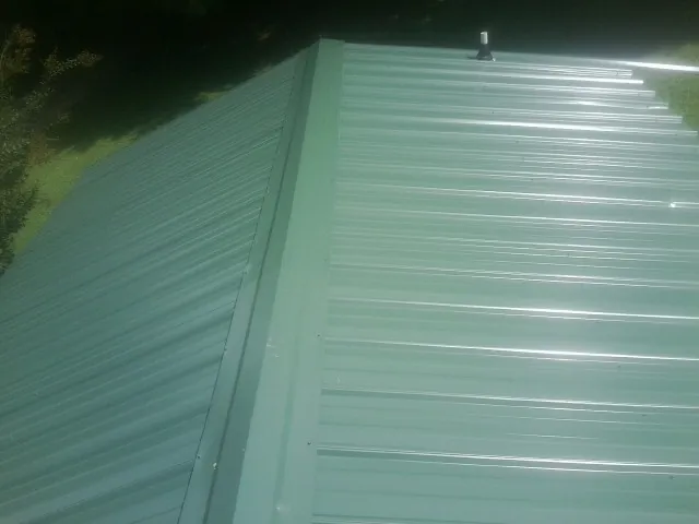 New green metal panels meeting at the ridge of a roof — Flat Roof Repair work by our crew in Cranbury