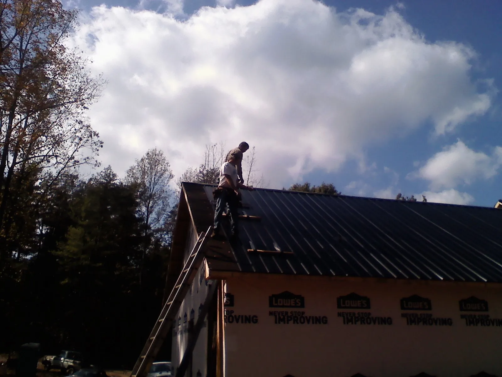 Roofer fastening dark metal panels high against a cloudy sky, from a Roof Inspection job in Cranbury