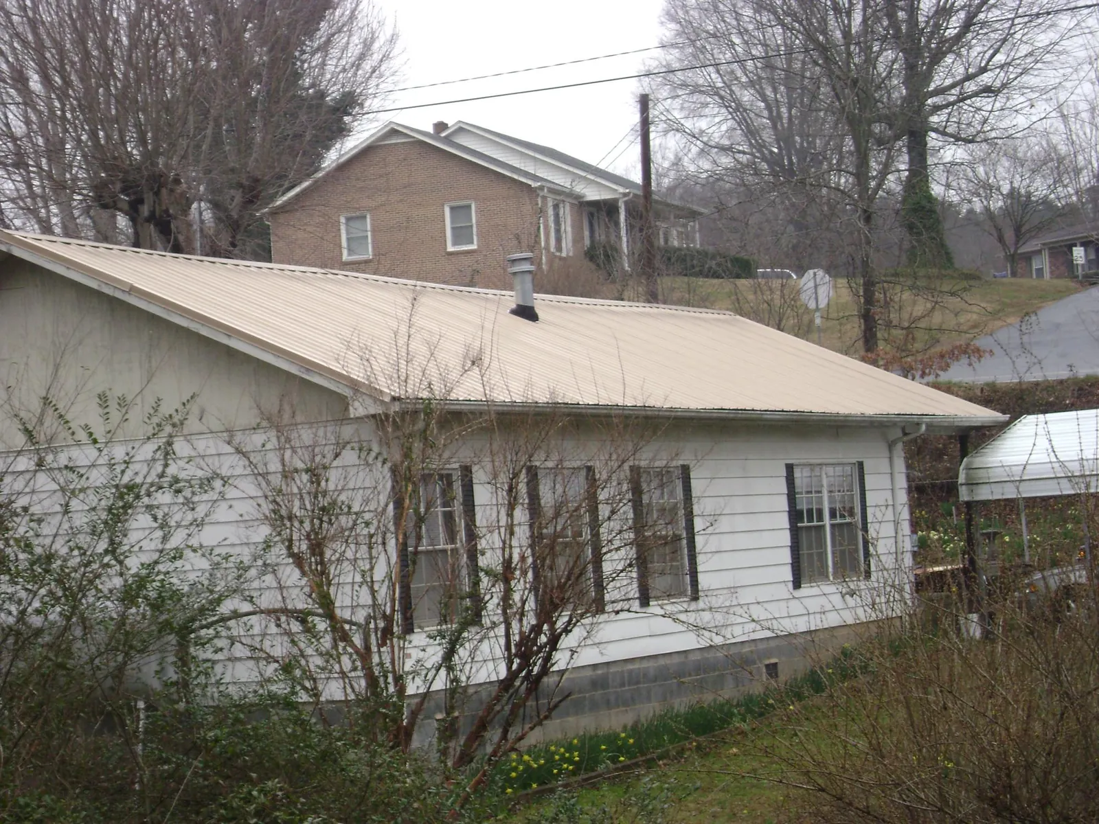 Tan metal roof on a white sided house set into a hillside — Commercial Roofing by Roofing Brothers in Cranbury